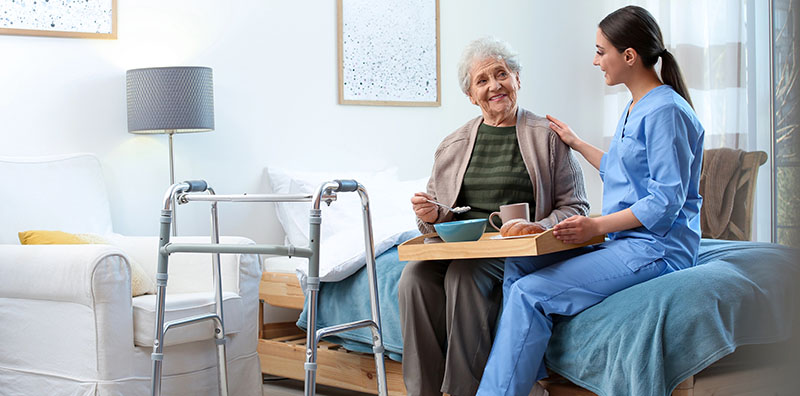 Care worker serving dinner for elderly woman in geriatric hospic
